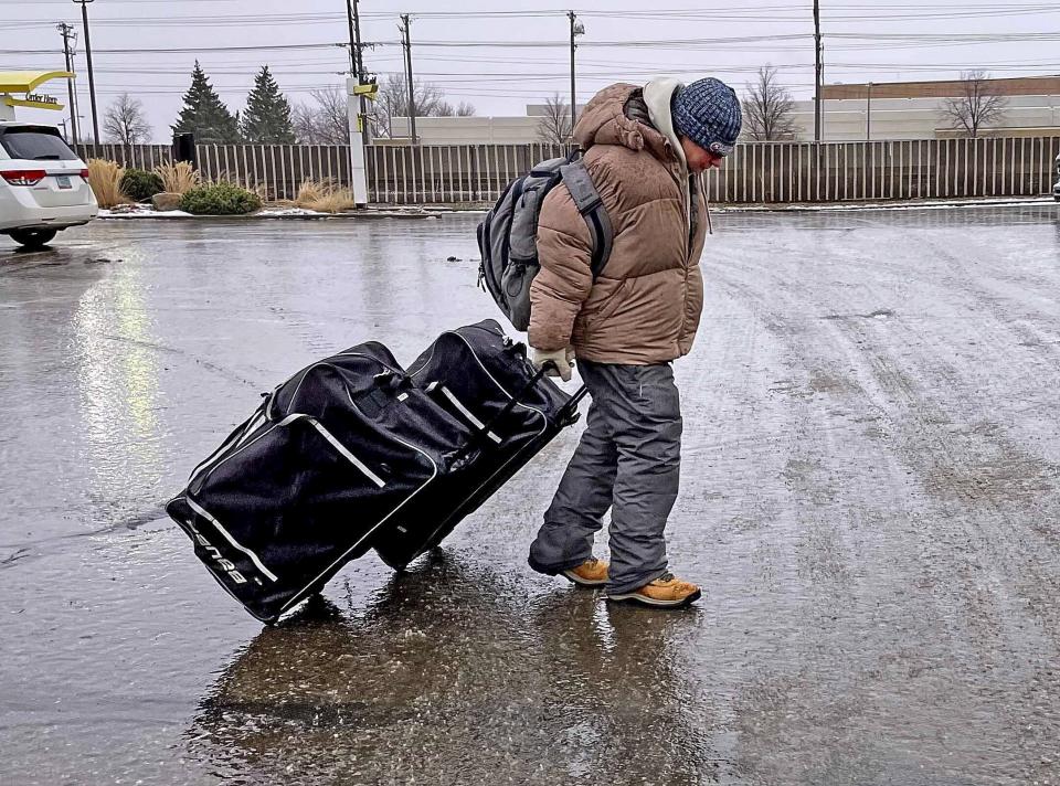 Brian Smith moves slowly pulling a pair of bags across an ice covered parking lot in downtown Bismarck, N.D., on Tuesday morning, Dec. 26, 2023, as ice covered streets and sidewalks made walking and driving difficult. (Tom Stromme/The Bismarck Tribune via AP)