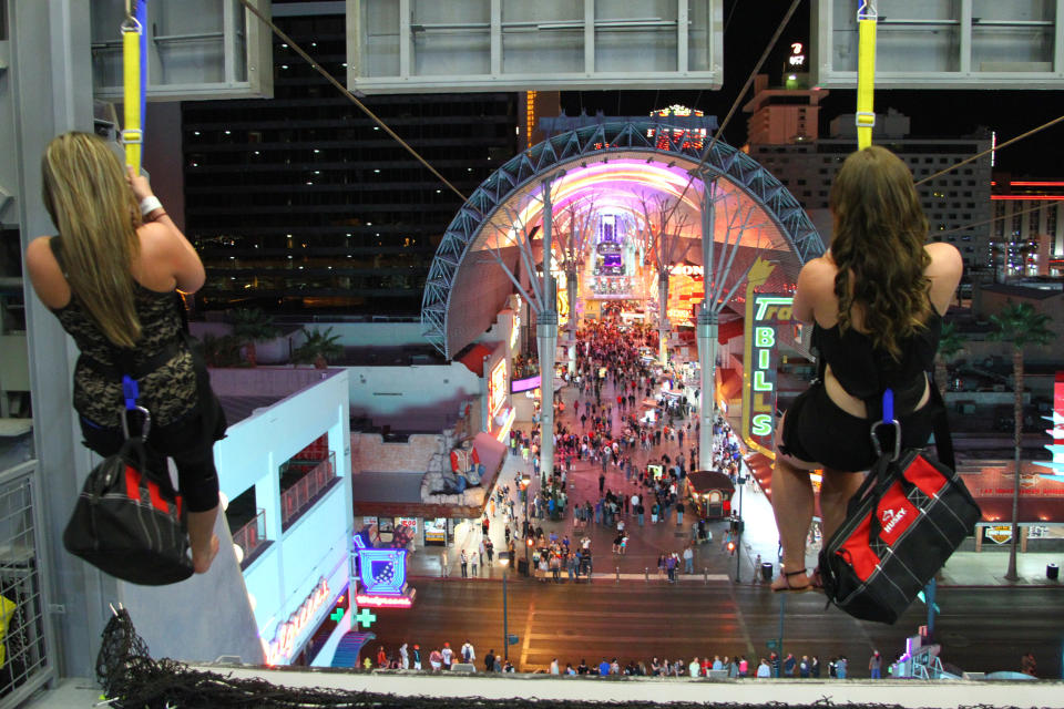 In this April 27, 2014 photo provided by the Fremont Street Experience, guests ride zip lines that swoop past the vintage casinos of downtown Las Vegas and under the giant video canopy of the Fremont Street Experience. The lower zip lines on the $12 million SlotZilla attraction opened over the weekend of April 26 after 14 months of construction. Rides start from a 12-story tower designed like a giant slot machine. Riders can now take the 77-foot-high zip lines, which harness visitors in a sitting position and take them 850 lateral feet to a platform near the 3rd Street Stage. (AP Photo/Fremont Street Experience, Scott Roeben)