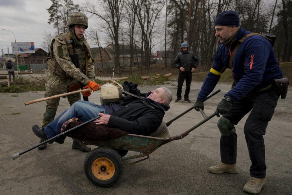 A man is helped in a wheelbarrow after crossing Irpin river on an improvised path under a bridge that was destroyed by Ukrainian troops designed to slow any Russian military advance, while fleeing the town of Irpin (AP)