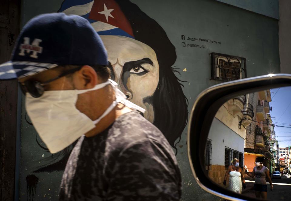 Un hombre con un cubreboca camina junto a un mural de Ernesto "Che" Guevara, mientras otras personas se reflejan en el espejo de un carro en La Habana, Cuba, el martes 7 de abril de 2020. Las autoridades cubanas han solicitado a las personas utilizar cubrebocas cuando salgan de sus casas como medida de precaución ante la pandemia del nuevo coronavirus. (AP Foto/Ramón Espinosa)