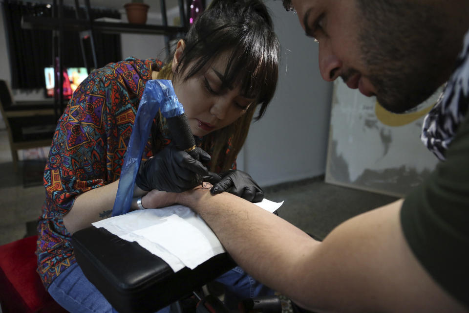 In this Saturday, 9, 2019, photo, Suraya Shaheedi, 26, Tattoo artist, left, pierced tattoo to a male customer in Kabul, Afghanistan. It’s been 18 months since Shaheedi started her mobile tattoo shop in the capital, Kabul. She’s received death threats for taking on the taboo of the ink-on-skin drawings she does — as well as being a single woman willing to work with men.. (AP Photo/Rahmat Gul)