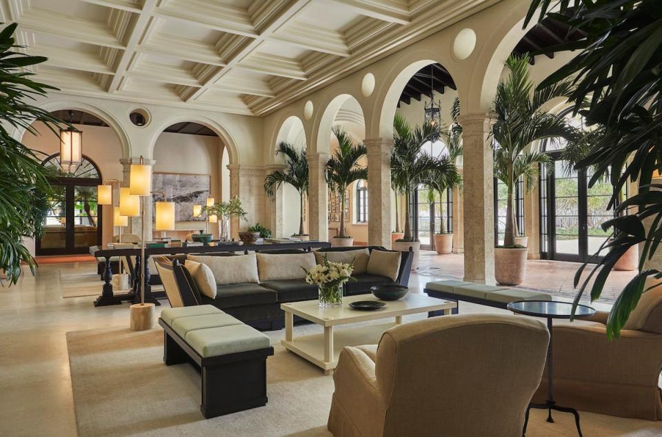 An interior photo of the lobby at The Four Seasons at the Surf Club shows couches and tables in a grand room with cream and walls and palm trees.