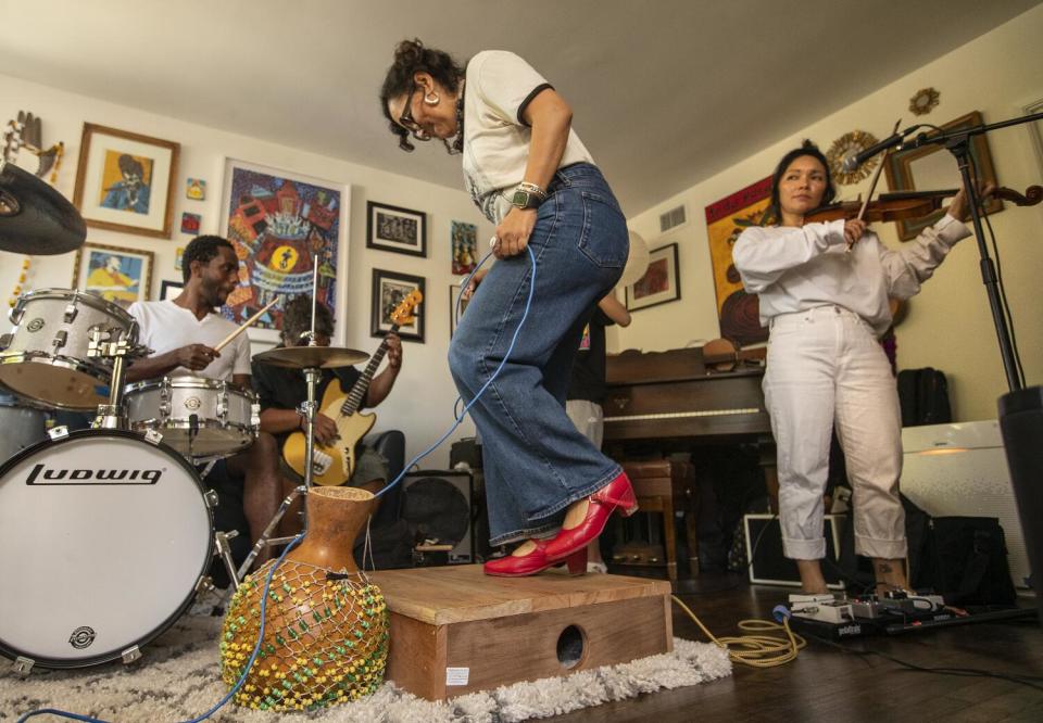 A woman in red shoes dances on a wooden platform as band members play their instruments around her.