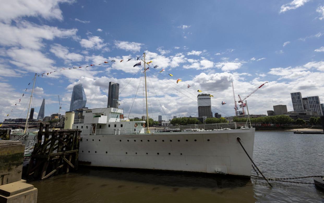 The white ship is seen on the Thames, against a bright blue sky, with central London behind it