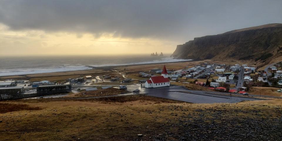 The town of Vik in southern Iceland. The photo shows a church, rows of houses, some streets, and mountains and sea in the background