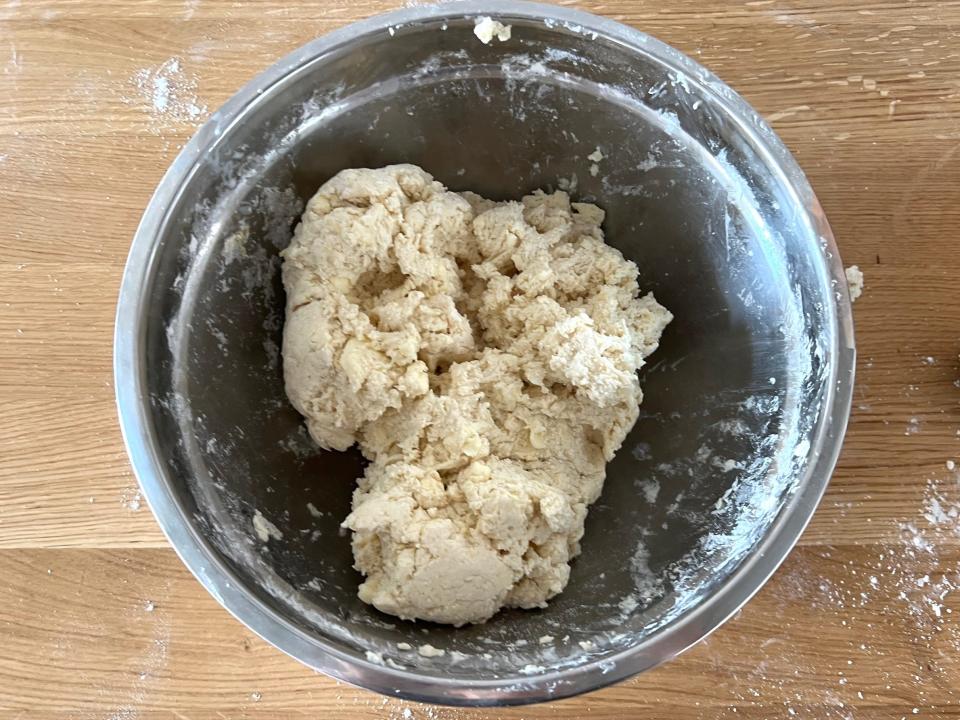 A silver bowl full of biscuit dough on a wood surface.