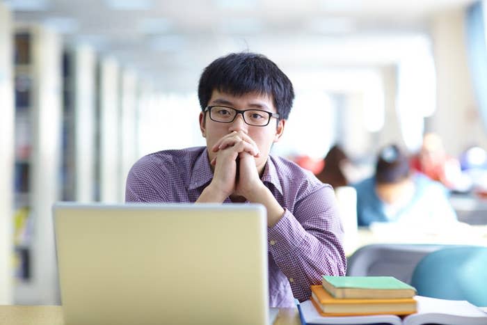 An Asian man staring off and looking contemplative in a classroom