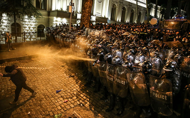 Georgian riot police spray tear gas towards a protester as they form a cordon