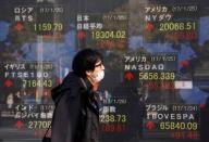 A man walks past an electronic board showing Japan's Nikkei average (top L), the Dow Jones average (top R) and the stock averages of other countries' outside a brokerage in Tokyo, Japan, January 26, 2017. REUTERS/Kim Kyung-Hoon