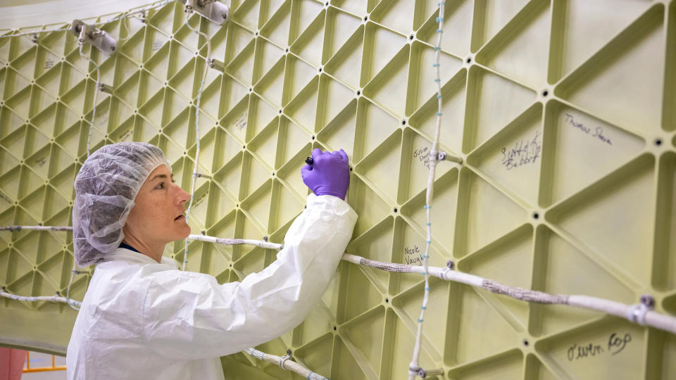 christina koch wears a cleanroom suit and hat and signs her name on a spherical, gridded rocket stage