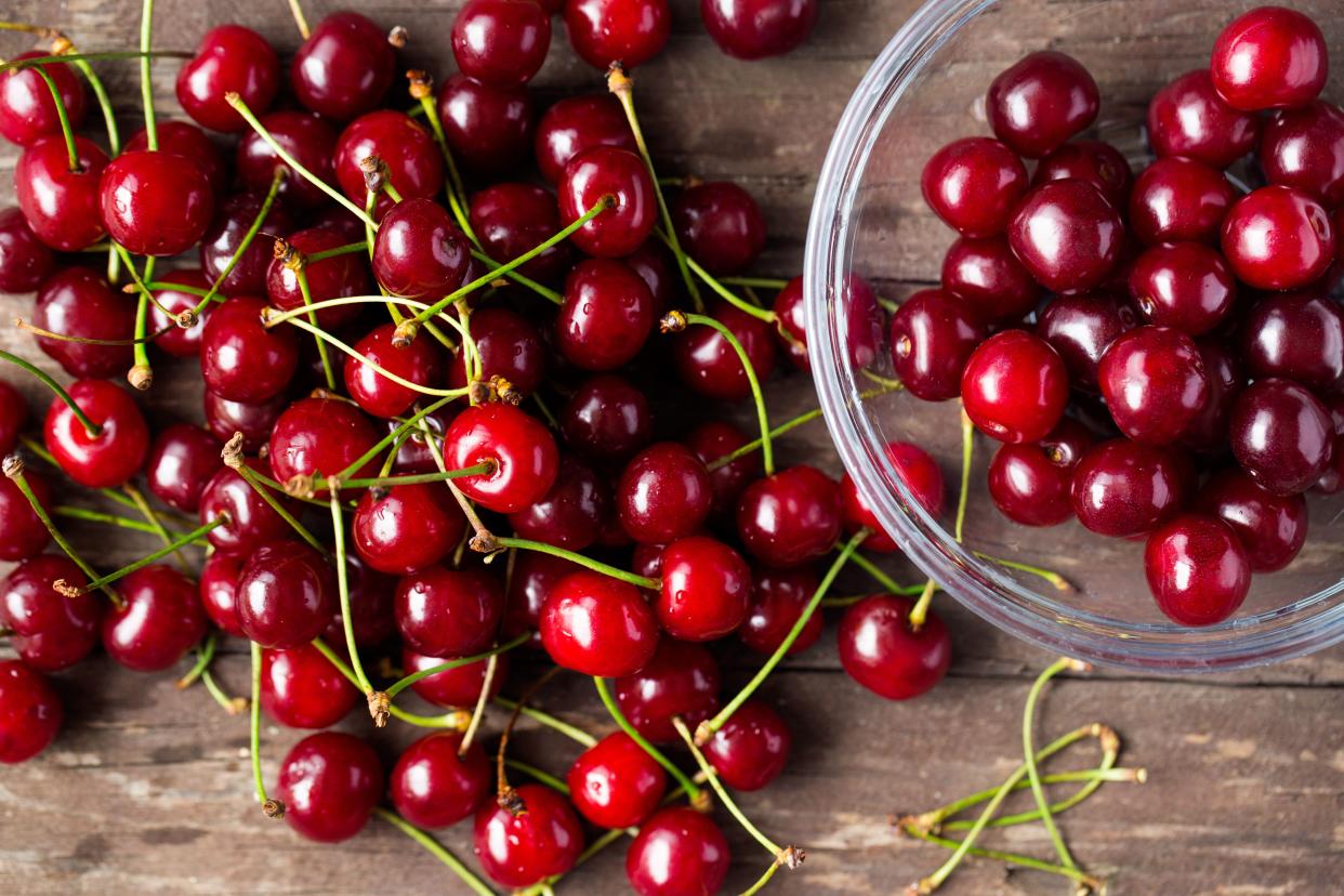 Fresh red cherries on a rustic wood table and in small glass bowl.