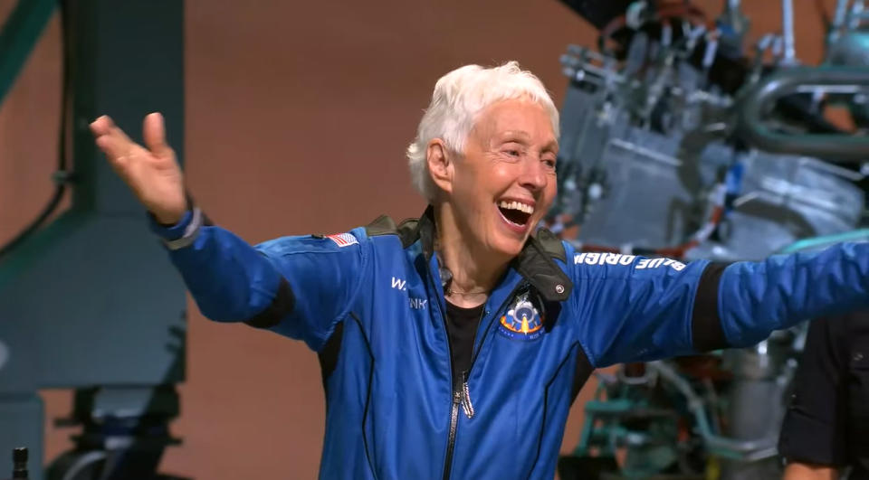 wally funk in a flight suit with arms outstretched, smiling widely