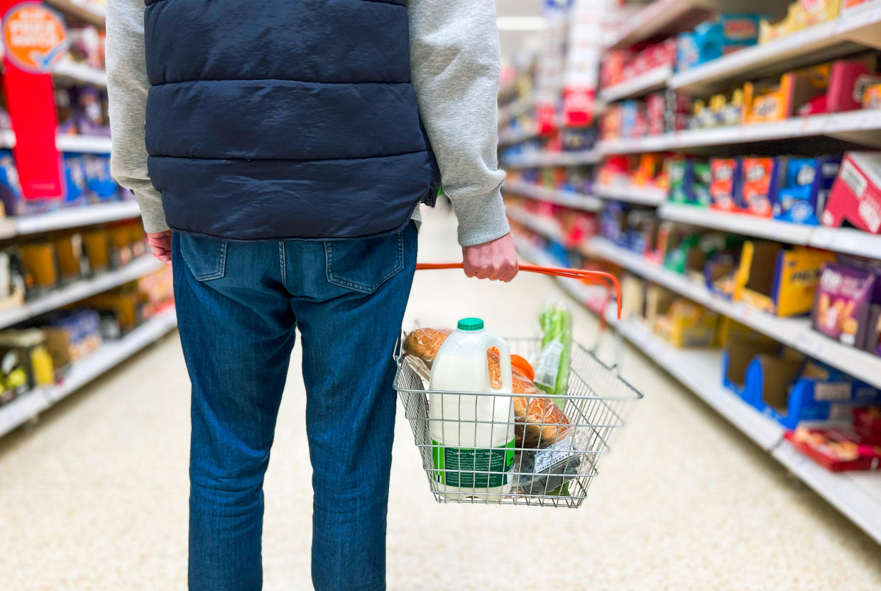  Man holding shopping basket with bread and milk groceries in supermarket. 