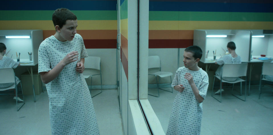 Eleven (Millie Bobby Brown) stares into a mirror and sees a de-aged version of herself - Credit: Courtesy of Netflix