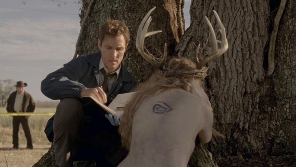Rust Cohle writes in his notebook near the corpse of a naked woman with antlers and a tattoo on her back in True Detective