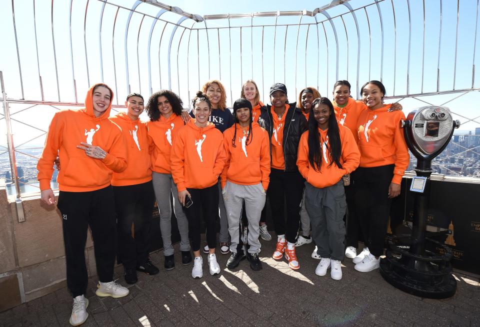 Members of the WNBA's 2022 draft class pose atop the Empire State Building while wearing the league's orange logo hoodies.