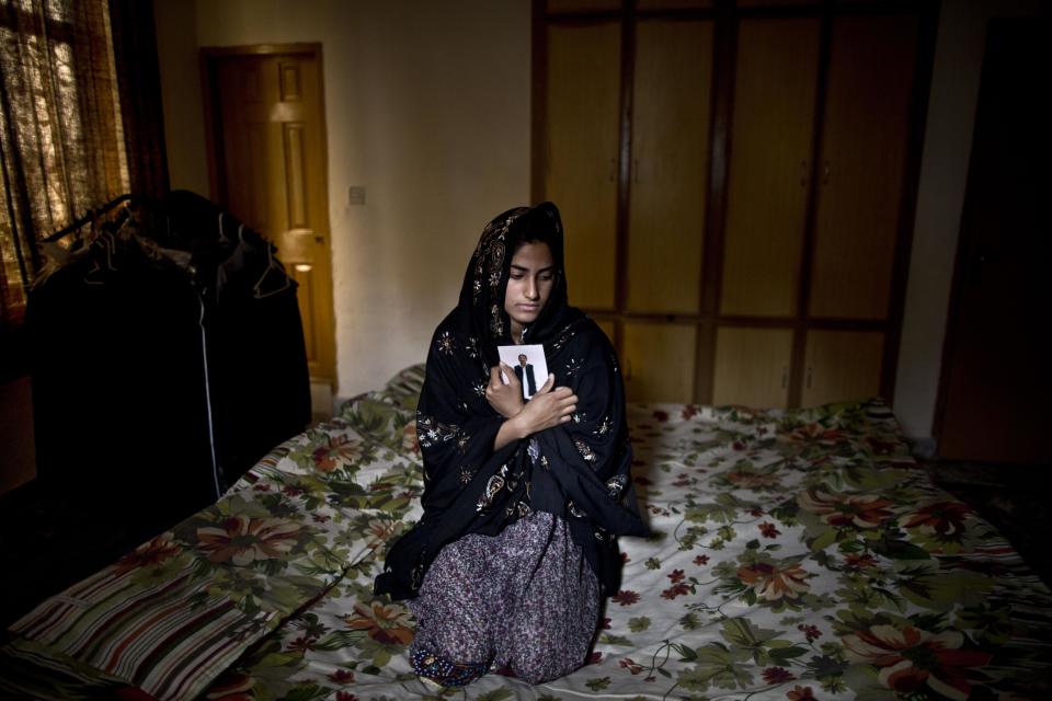 In this Sunday, March 16, 2014 photo, Pakistani Syeda Aima Tanveer, 20, daughter of lawyer Tanveer Haider, 58, who was one of eleven victims that was killed by suicide bombers in an attack on a court complex on the 3rd of March 2014, sits on her father's bed embracing his photograph, at their home on the outskirts of Islamabad, Pakistan. "My father, my hero, I miss you so much father," Aima said. (AP Photo/Muhammed Muheisen)