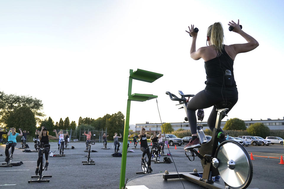 Cycle spinning instructor Alli Sherman, of Newburyport, Mass., top right, leads a spinning class in a parking lot outside Fuel Training Studio, Monday, Sept. 21, 2020, in Newburyport. The gym's revenue is down about 60% during the COVID-19 pandemic. Fuel Training Studio plans to continue holding outdoor classes into the winter with the help of a planned greenhouse-like structure with heaters but no walls. (AP Photo/Steven Senne)