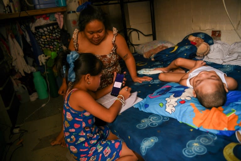 Cindella Manabat (C) helps her daughter Ella Araza (L) with homework, at their house in Manila (Ted ALJIBE)