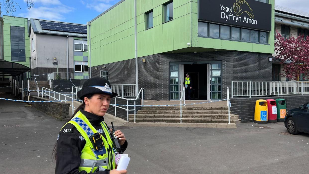 A female police officer stands in front of the school