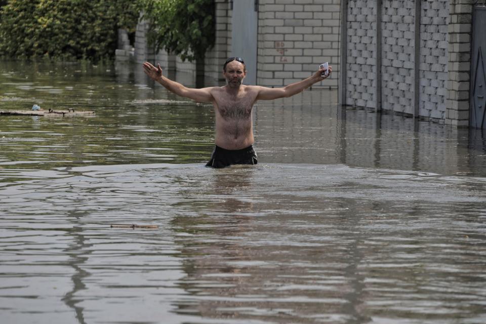 man stands shirtless in floodwaters up to his waist with his arms spread out