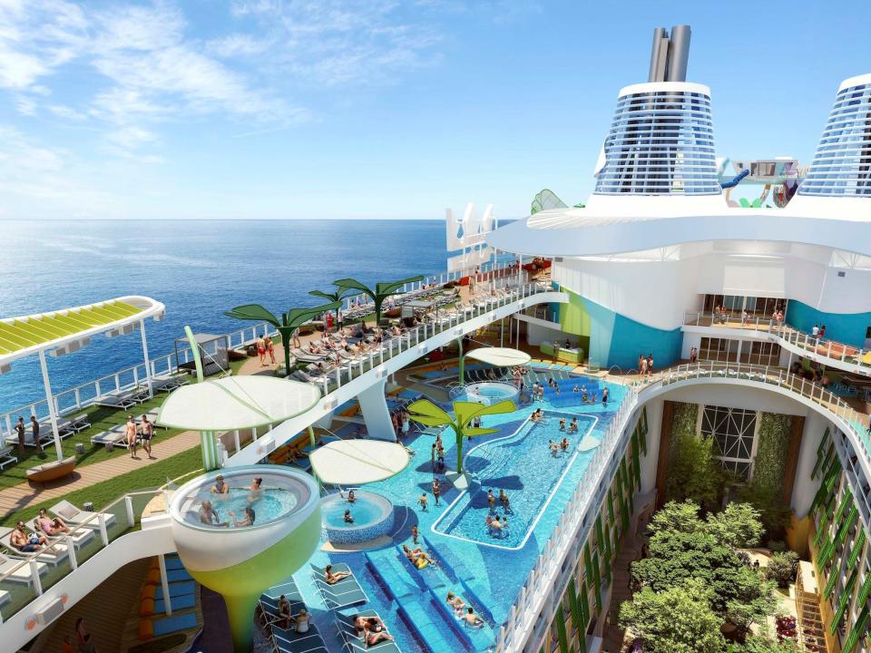 A view of the top deck of the Icon of the Seas which has a large swimming pool with chairs that rise out of the water and a top deck that has a green lawn with multiple sun loungers.