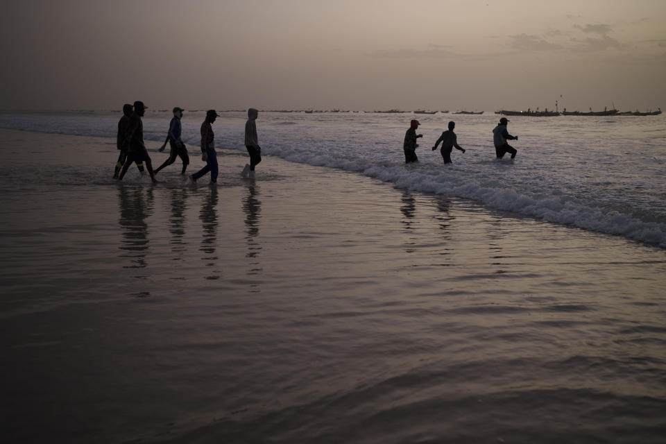 Un grupo de pescadores jóvenes camina hacia el mar para subir a una embarcación tradicional de pesca, en Nuakchot, Mauritania, el 10 de diciembre de 2021. (AP Foto/Felipe Dana)