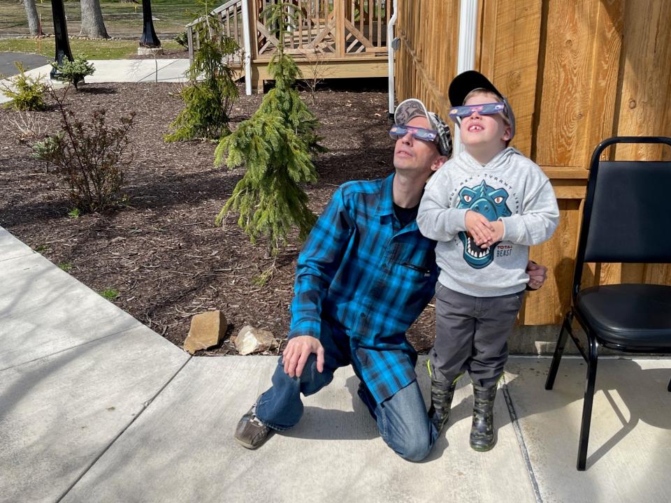 Brandon Smalley and his son, Finn, of Johnstown, watch the solar eclipse from the sidewalk outside the Grand Ballroom.
