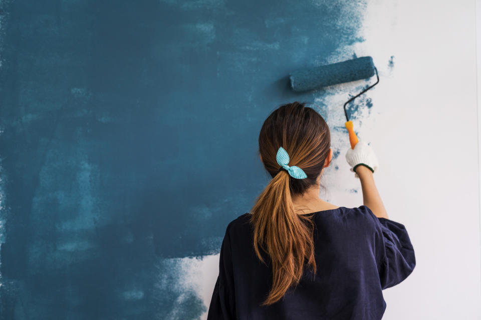 Woman painting a room blue with a paint roller.