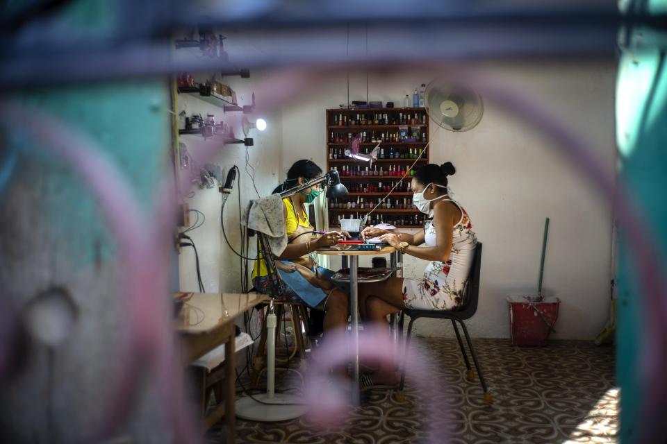 Two women wearing masks as a precaution against the spread of the new coronavirus paint their nails at a home nail salon in Havana, Cuba, Tuesday, March 31, 2020. Cuban authorities are requiring the use of masks for anyone outside their homes. (AP Photo/Ramon Espinosa)