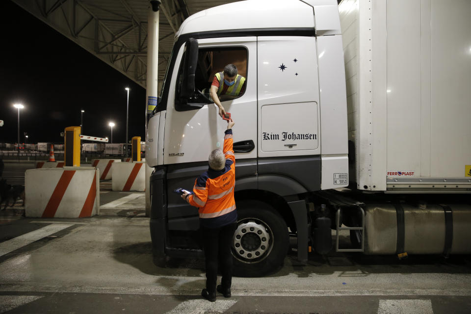 A man gives a document to the driver of the first truck, from Estonia, entering the Eurotunnel terminal Friday, Jan.1, 2021 in Coquelles, northern France. Eleven months after Britain's formal departure from the EU, Brexit becomes a fact of daily life on Friday, once a transition period ends and the U.K. fully leaves the world's most powerful trading bloc. (AP Photo/Lewis Joly, Pool)