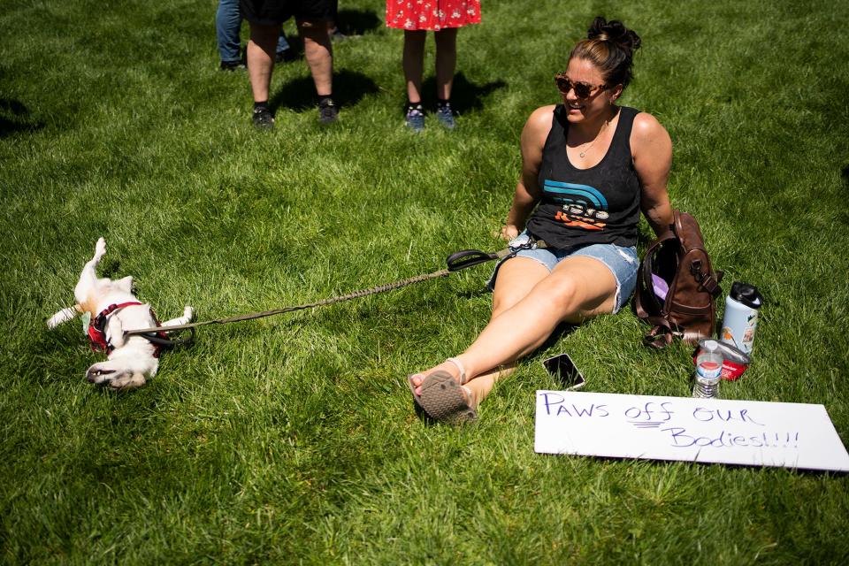 Kenzie Kanney, of New Albany, sits in the grass with her dog, Rocky, and a sign that reads "Paws off our Bodies" at Planned Parenthood Advocates of Ohio's "Ban Off Our Bodies" rally Saturday at the Ohio Statehouse.