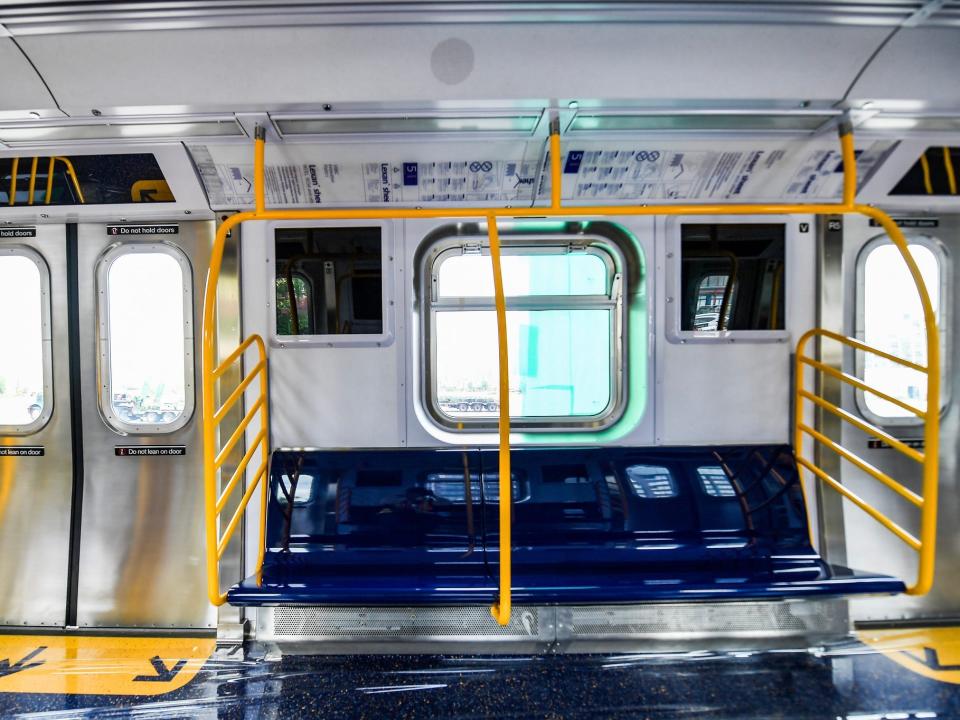 Inside the brand new subway fleet with dark blue seating, Yellow poles and railings, and windows with light coming through