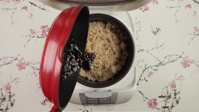 Pouring sauce from frying pan into brown rice in rice cooker