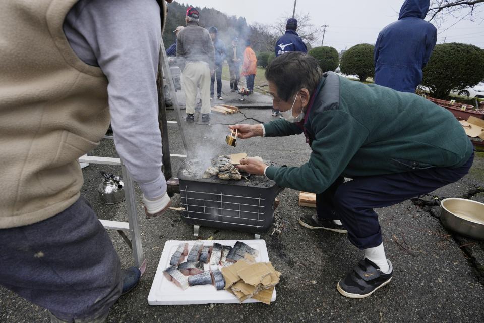 An evacuee volunteers to grill pieces of fish at a temporary evacuation center in Suzu in the Noto peninsula facing the Sea of Japan, northwest of Tokyo, Wednesday, Jan. 3, 2024, following Monday's deadly earthquake. (AP Photo/Hiro Komae)