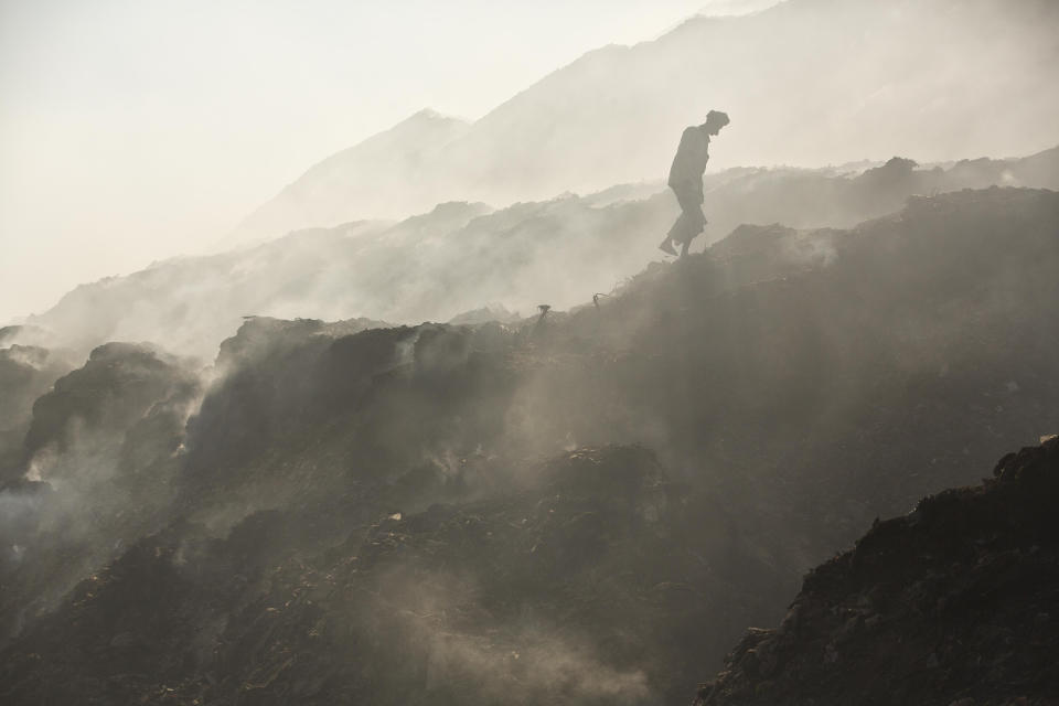 In this Monday, Dec. 10, 2018 photo a ragpicker man walks amidst the smoke to search recyclable materials at a garbage dumping site on the outskirts of Gauhati, India. (AP Photo/Anupam Nath)