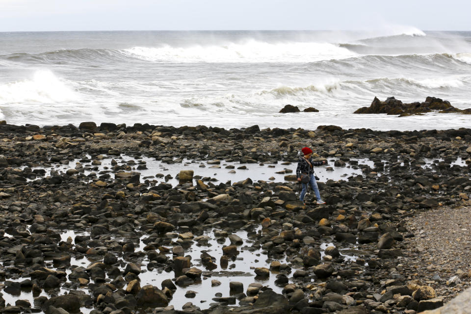 A woman walks along the rocks near waves from Lee, Saturday, Sept. 16, 2023, in Rye, N.H. The storm is expected to make landfall Saturday in Canada at near hurricane strength and then move farther into the region. (AP Photo/Caleb Jones)