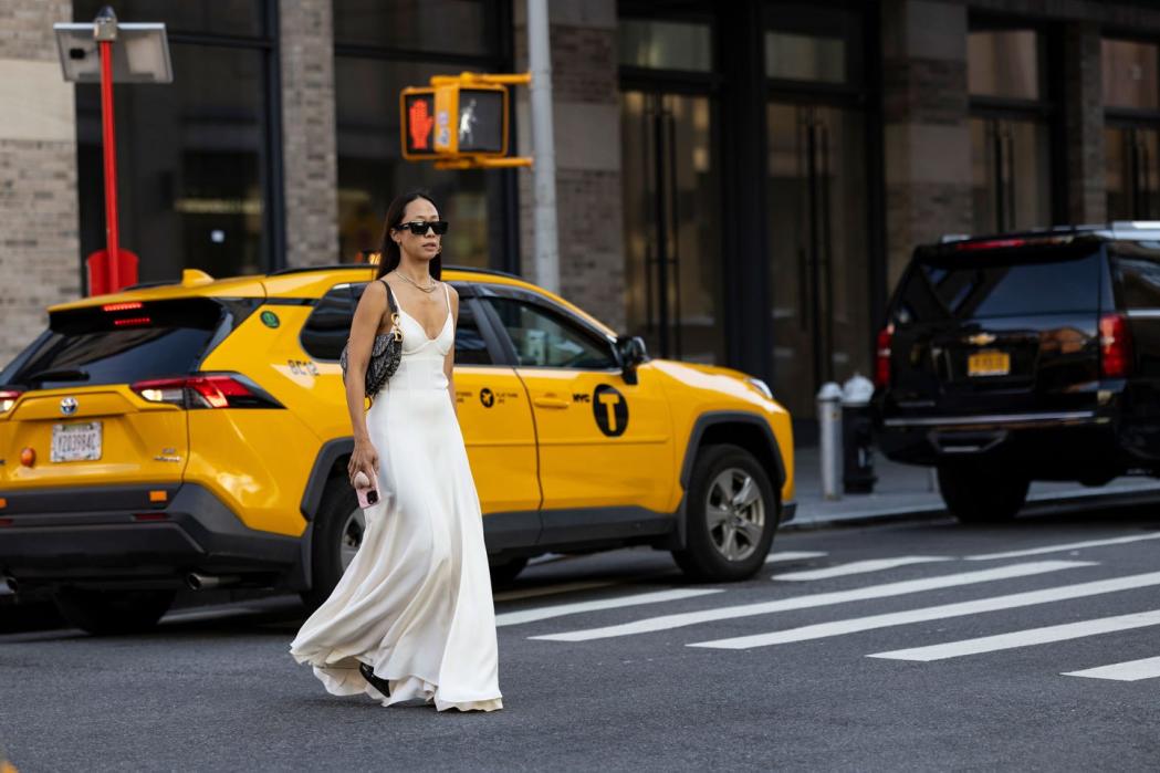 a person in a white dress and sunglasses standing in the middle of a street