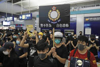 Demonstrators holding a placard with defaced Hong Kong Police insignia reading in Chinese "White Terror", stand in silence during a protest at the Yuen Long MTR station in Hong Kong, Wednesday, Aug. 21, 2019. Hong Kong riot police faced off briefly with protesters occupying a suburban train station Wednesday evening following a commemoration of a violent attack there by masked assailants on supporters of the anti-government movement. (AP Photo/Kin Cheung)