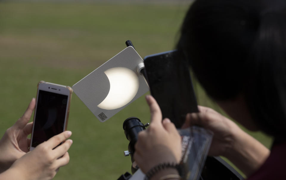 Students take a picture of a reflection of a partial solar eclipse at a school in Bangkok, Thailand, Thursday, Dec. 26, 2019. (AP Photo/Sakchai Lalit)