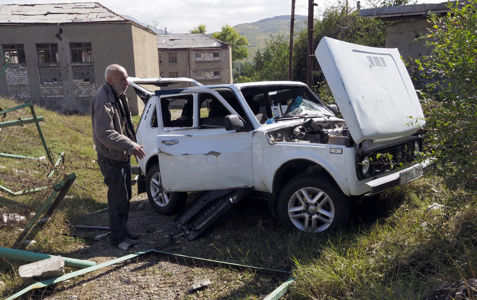 A man stands near a car damaged by shelling by Azerbaijan's artillery, during a military conflict in Stepanakert, the separatist region of Nagorno-Karabakh, Saturday, Oct. 10, 2020. Armenia and Azerbaijan have agreed to a Russia-brokered cease-fire in Nagorno-Karabakh after two weeks of heavy fighting that marked the worst outbreak of hostilities in the separatist region in more than a quarter-century. (AP Photo)