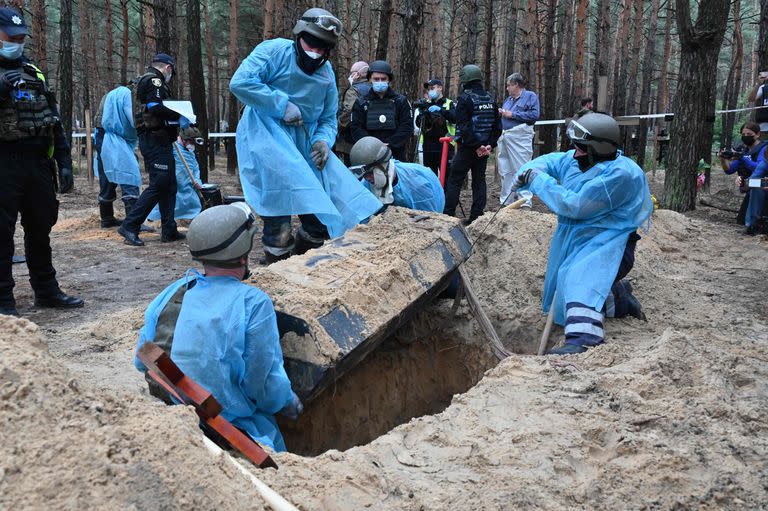 Un técnico forense inspecciona un cuerpo en un bosque en las afueras de Izium. (Photo by SERGEY BOBOK / AFP)