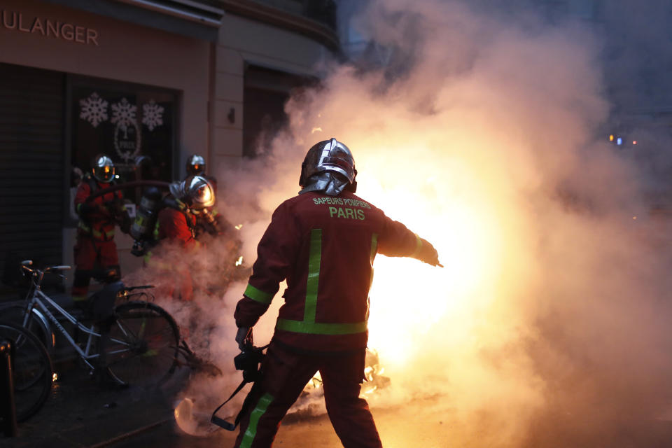 Los bomberos intentan extinguir el fuego de un vehículo incendiado por manifestantes durante un enfrentamiento con policías antidisturbios en París, el sábado 8 de diciembre de 2018. (AP Foto/Thibault Camus)