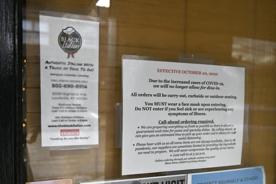 Signs on the door of The Black Italian restaurant and catering service showing the COVID-19 restrictions, in Louisville, Ky., Thursday, Dec. 3, 2020. The restaurant's owners, Paula and Anthony Hunter cannot have in person dining, and are hoping for another round of federal aid to hang on until vaccines can conquer the virus. (AP Photo/Timothy D. Easley)