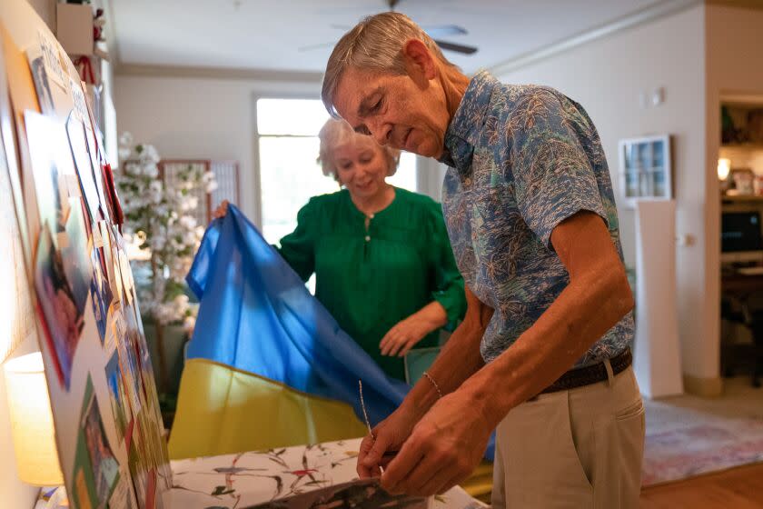 MAITLAND, FL - FEBRUARY 15: Greg Dawson (right) looks at old family photos and memorabilia while his wife, Candy Dawson, watches as she holds the Ukraine flag on Wednesday, Feb. 15, 2023 in Maitland, FL. (Sydney Walsh / For The Times)