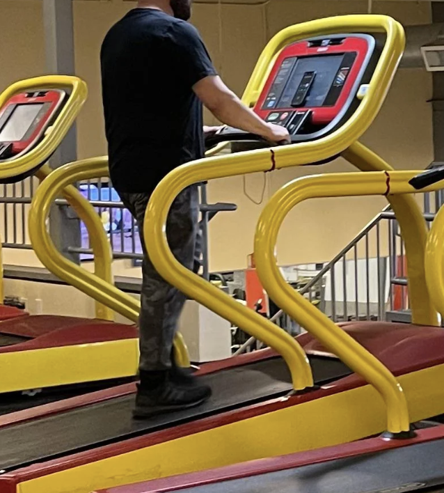 A person walks on a treadmill at a gym. The treadmill has yellow and red accents