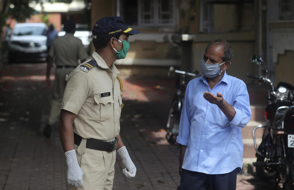 A police officer speaks with the watchman of the building where Bollywood actor Sushant Singh Rajput lived in Mumbai, India, Sunday, June 14, 2020. Rajput was found dead at his Mumbai residence on Sunday, police and Indian media reports said. (AP Photo/Rafiq Maqbool)