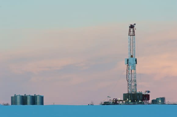 A natural gas drilling rig at dawn in a snowy field.