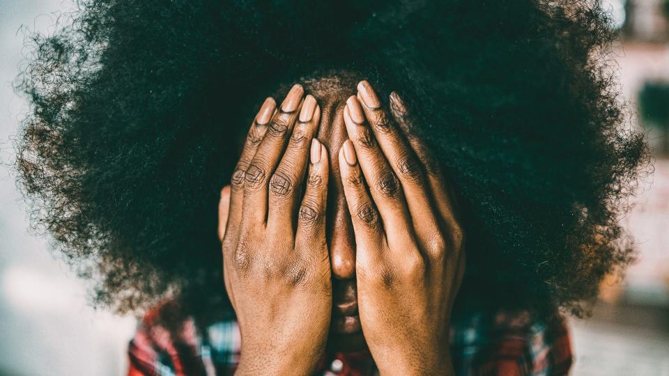 African woman hiding her face with hands.