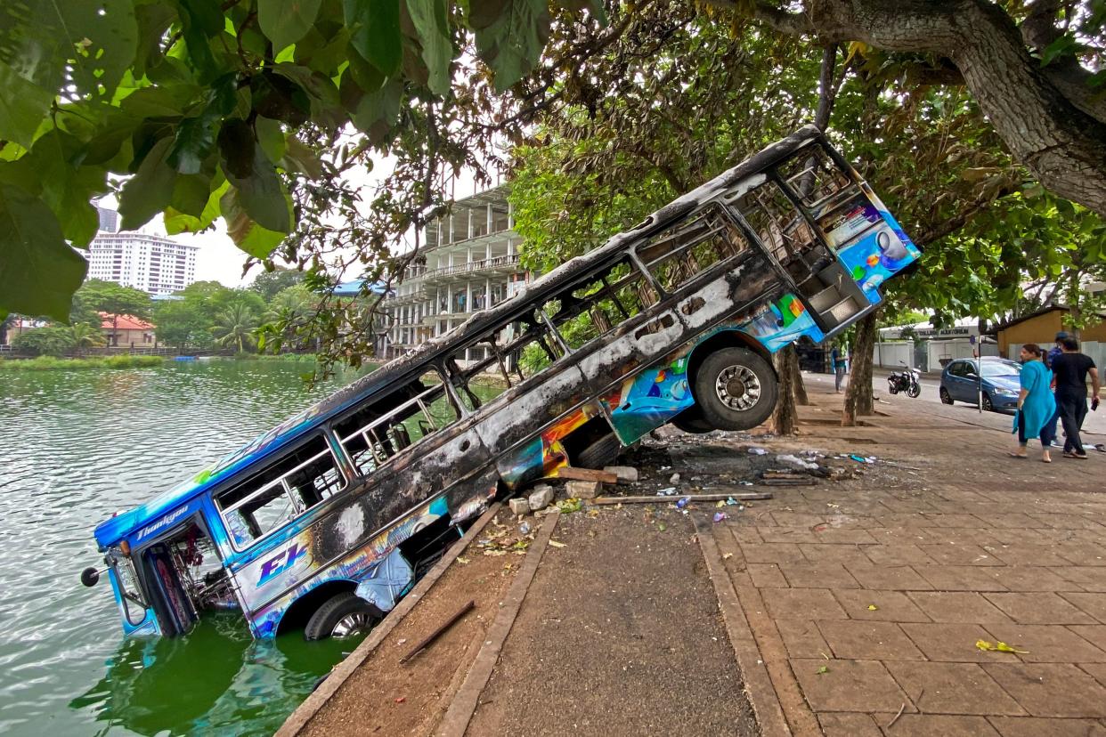 A burnt blue bus tipped at a rakish angle into the water off a quay.